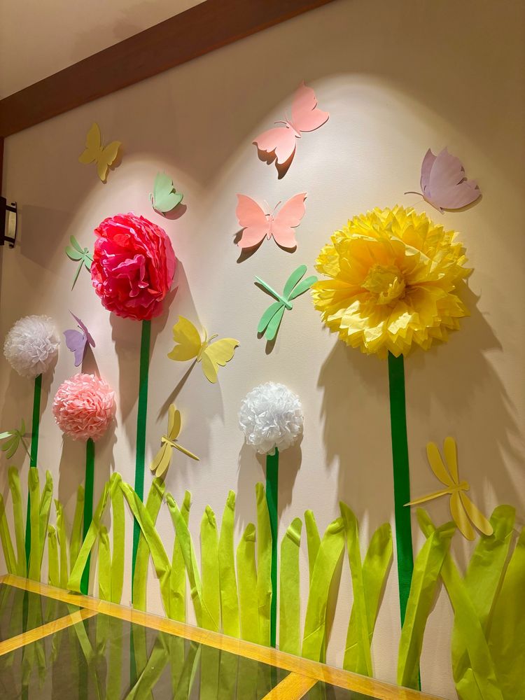 Paper flowers, grass, and butterflies on a wall.