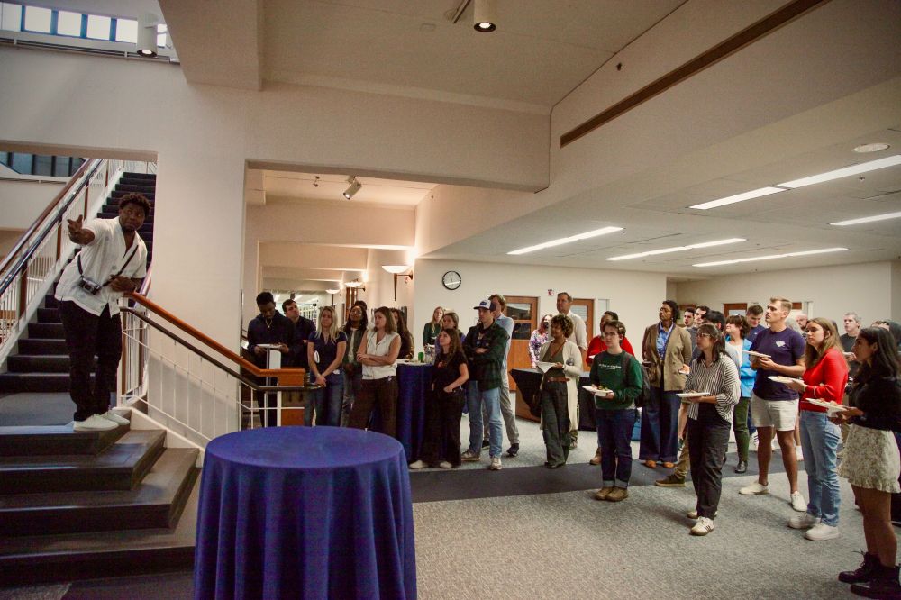 Eze Amos standing on a stairwell platform, gesturing off of frame, while speaking to a small crowd.