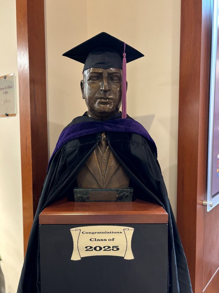 A bust of Arthur J. Morris wearing a cap, gown, and hood. There is a sign that reads “congratulations class of 2025.”