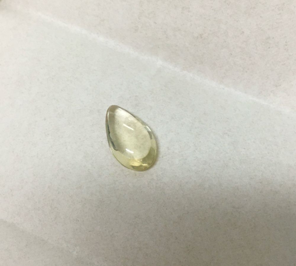 Transparent yellow pear shaped cabochon on white paper. At the Canadian Museum of Nature.