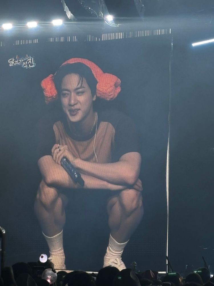 Seokjin on stage in Dallas. He's in his spa/water park fit which includes shorts. He's squatting down and showing off some serious leg.