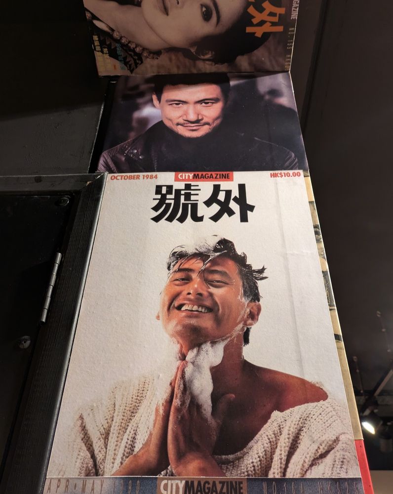 Un montant de mur recouvert de unes de magazines.
Dont une qui expose fièrement Chow Yun Fat dans toute sa splendeur en plein shampooing. Il est content. Il porte un pull. Il est magnifique.