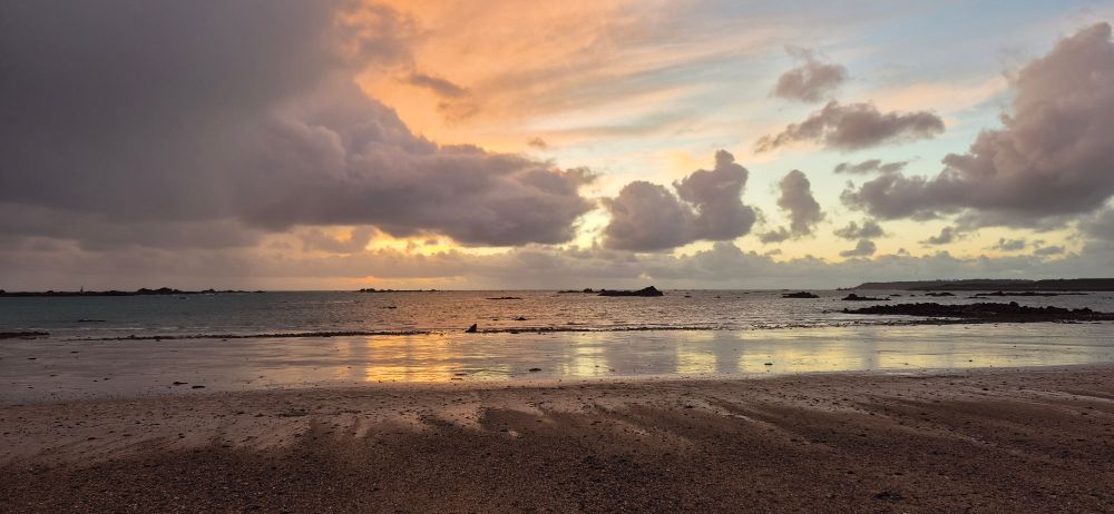 The start of sunset over s beach. Silver water. Blue and orange sky. Wet sand as the tide goes out.