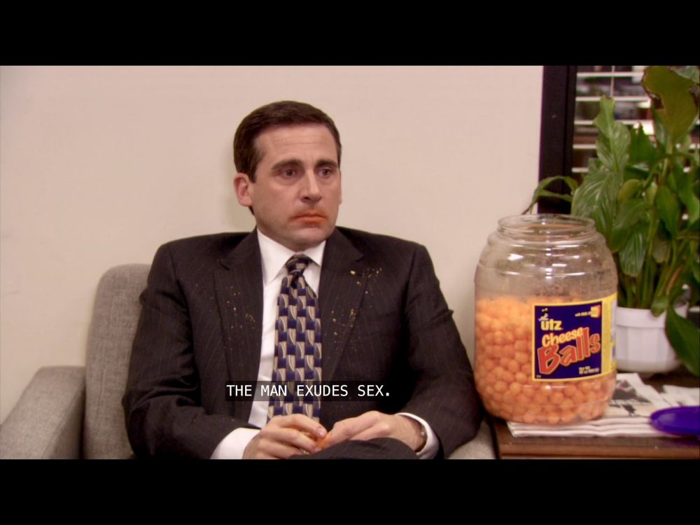 Michael Scott from the Office sitting in a chair, eating cheese balls, with cheese ball residue all over his face

Caption: "the man exudes sex"