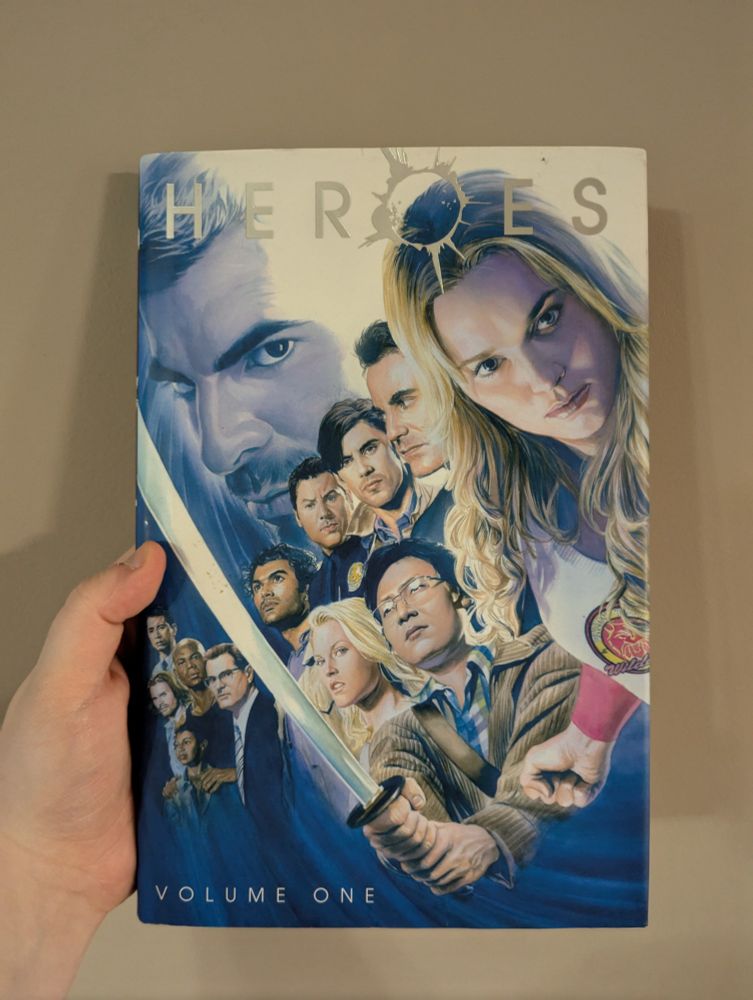 A hand holding a hardback volume one of "Heroes" based on the hit 2006 TV show by the same name
