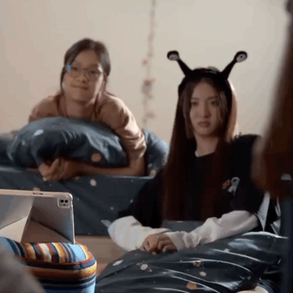 two girls are laying on a bed with one wearing a headband that looks like an alien