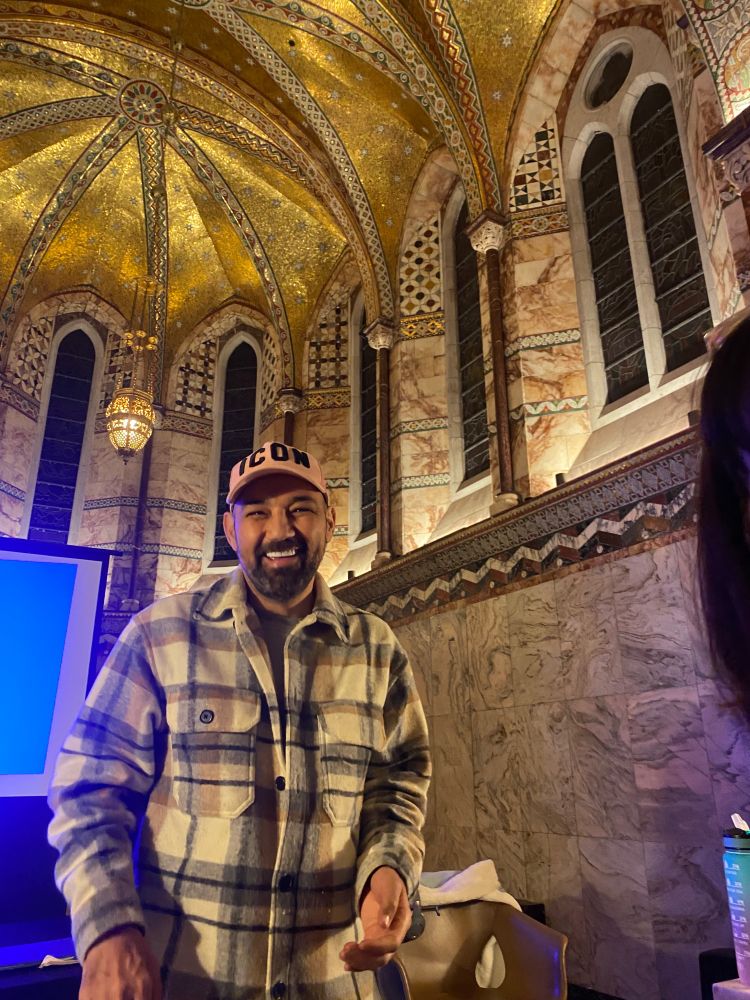 The golden ceiling of The Fitzrovia Chapel in London shining bright with intricate details, bottom left is Stephen Hart in a checked shirt with a pink baseball cap that read ICON