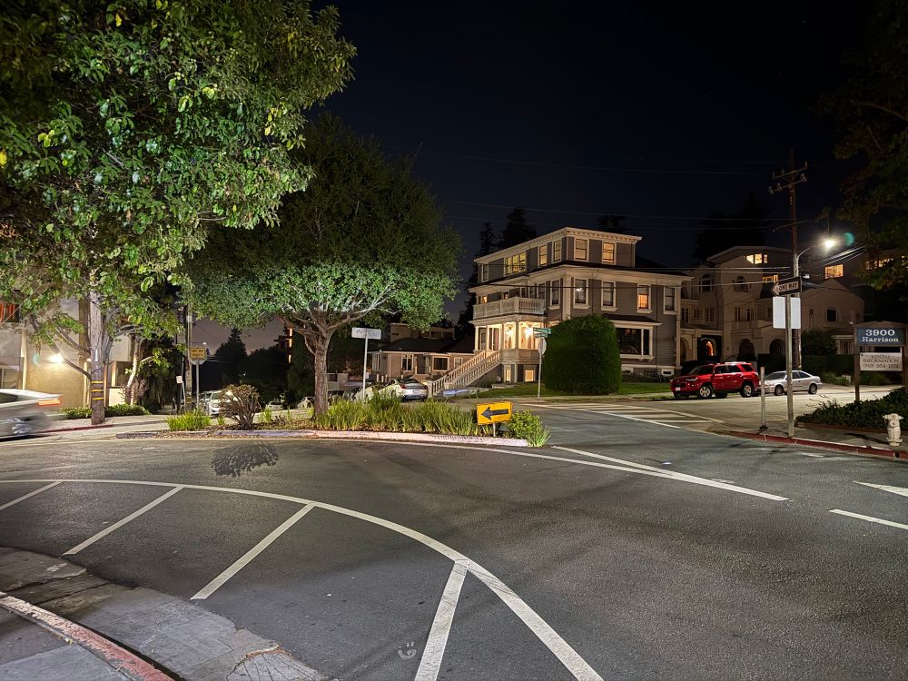 An Oaklamd intersection in a high density residential neighborhood at night. A high speed turn lane connects westbound Bayo Vista Avenue with southbound Harrison Street. No crosswalks connect the southeast corner with the other sides of the street. 