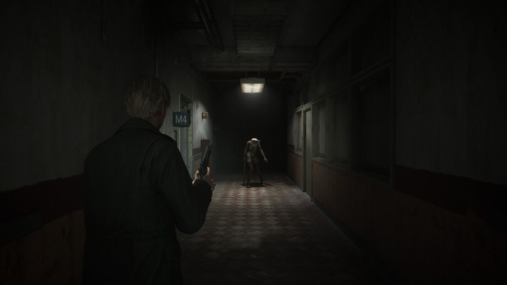 A still from the Silent Hill 2 remake. The protagonist readies a handgun as a bubble head nurse waits further down a darkened hospital hallway. 