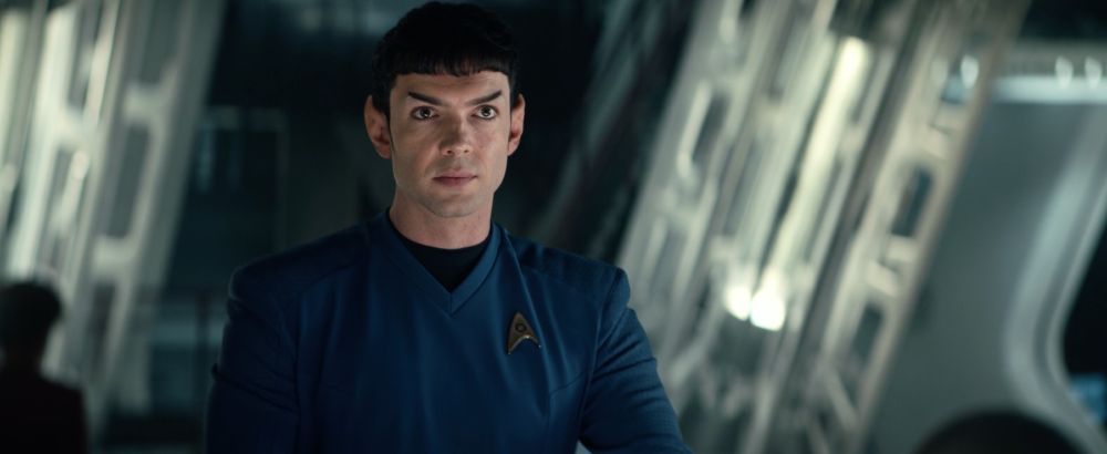 Ethan Peck as Mr Spock on Star Trek Strange New Worlds. Standing in the engineering section of the Enterprise. Spock is wearing a blue uniform and has pointed Vulcan ears. Screenshot from Season 2 Episode 9 "Subspace Rhapsody"