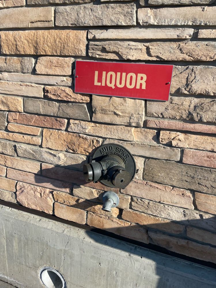 A large two-headed hose attachment on the exterior of a commercial building, labelled ‘liquor’ for some reason.