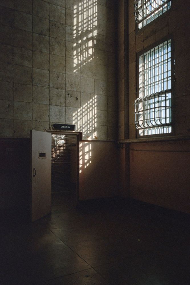 An open door with a sign above it that says “Library”. Two windows to the right of it let in sunlight to the walls. 