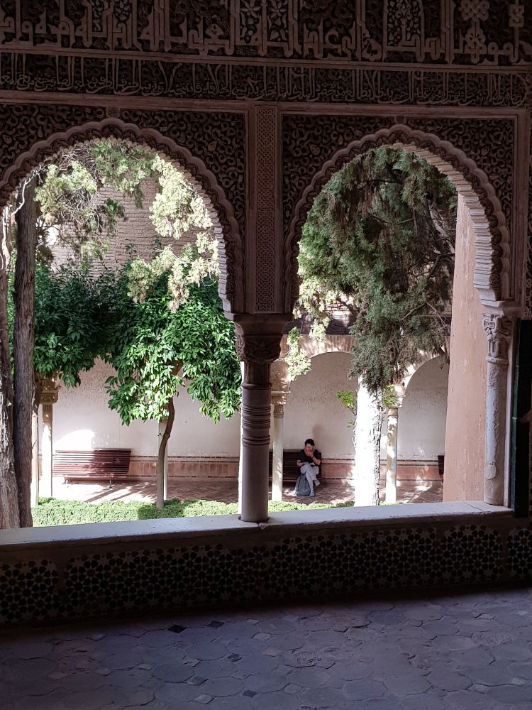 durch das fenster blick auf den innenhof. eine frau sitzt auf einer bank, bäume