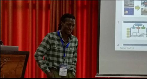 Edwards lab graduate student Eugene Gyasi Agyemang beside a podium in front of a presentation.