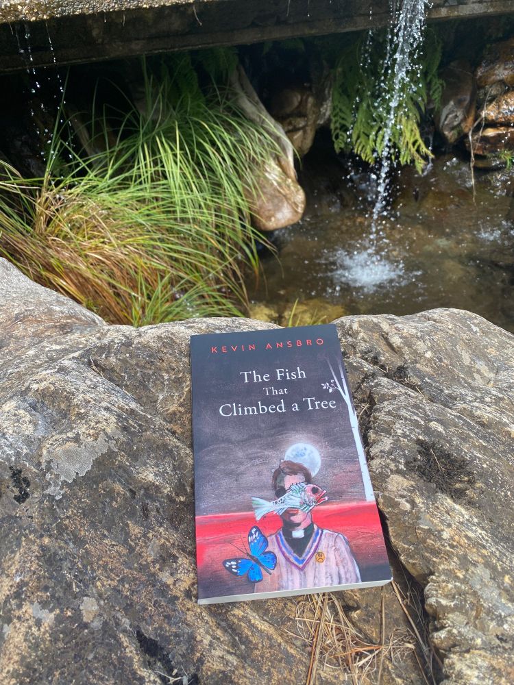 Kevin Ansbro's book, The Fish That Climbed A Tree, on top of a rock near some bushes under a bit of running water (not big enough to be a waterfall).