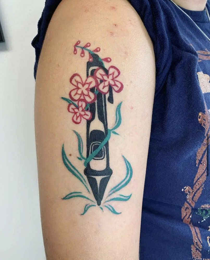A photo of a tattoo. The design is of a stylus pen with fireweed blooming out of the tip and around the pen, all in the style of formline art.