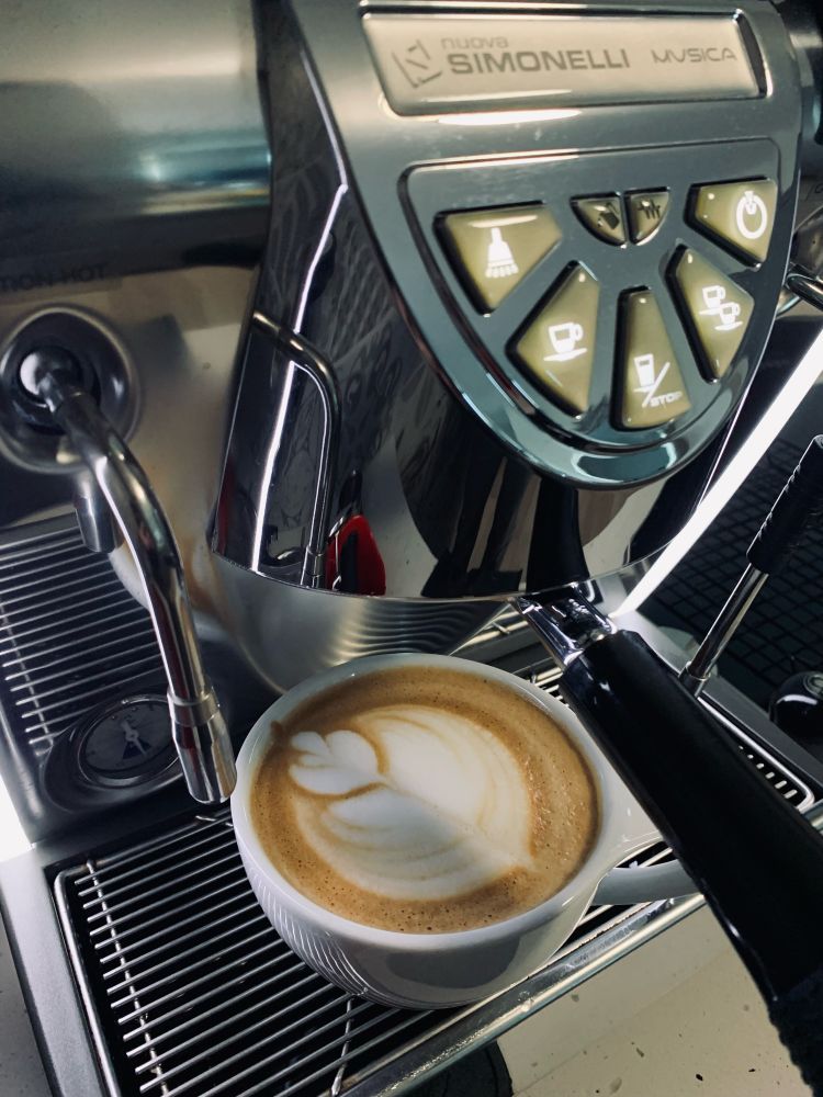 Cup of coffee with latte art, sitting on top of the drip tray of a espresso machine.