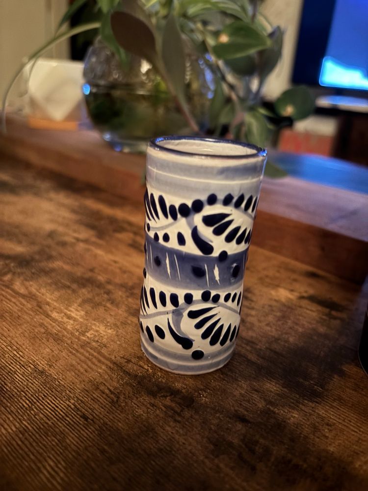 A ceramic shot glass of white with blue designs 