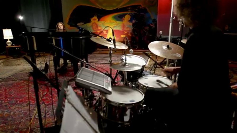 a man playing drums in a dark room with a woman behind him