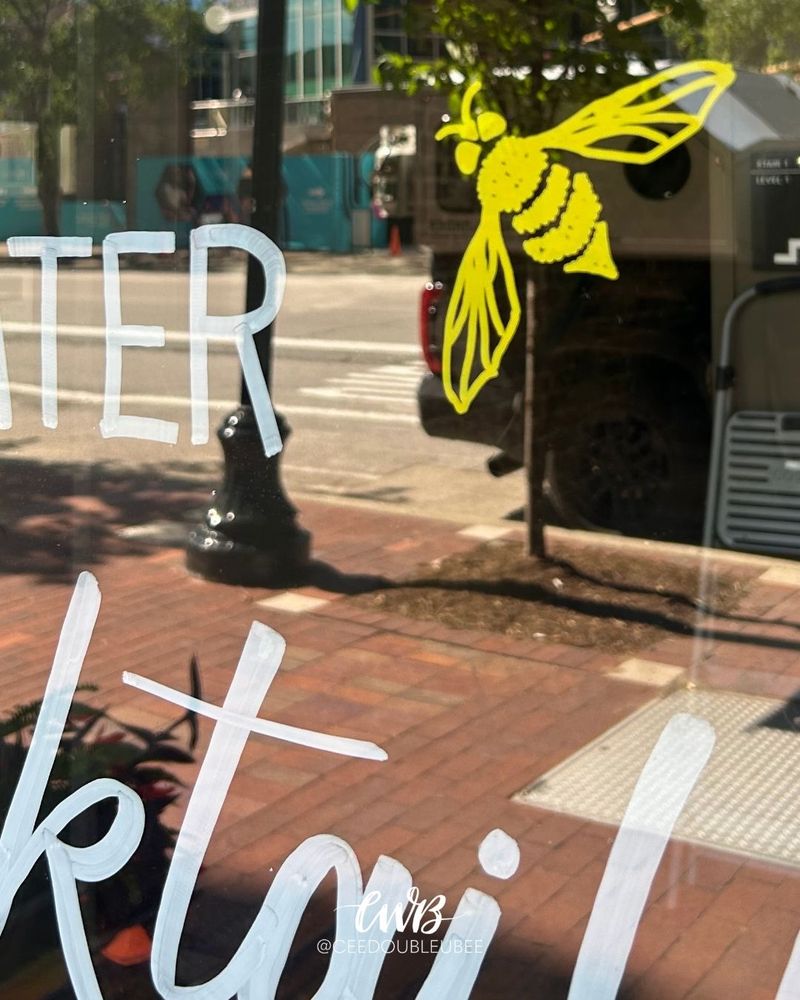 Hand lettered summer window display featuring a Honey Lavender Lemonade cocktail recipe for Evan Williams Bourbon Experience. Includes a detailed illustration of the drink and matching bees near the bottle branding.