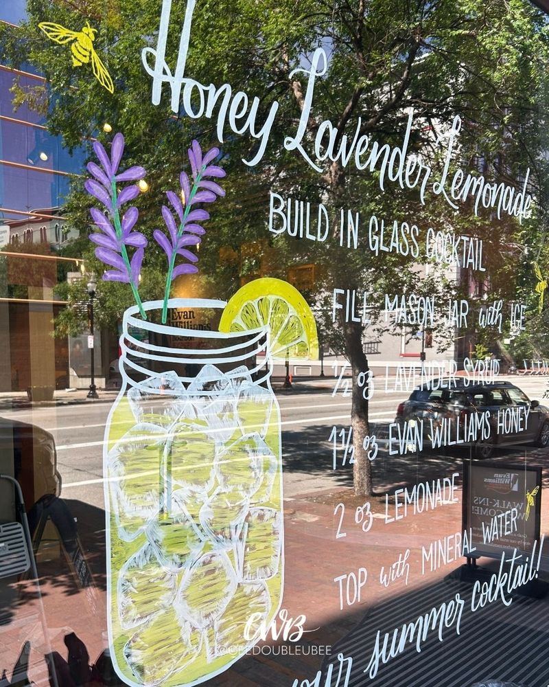 Hand lettered summer window display featuring a Honey Lavender Lemonade cocktail recipe for Evan Williams Bourbon Experience. Includes a detailed illustration of the drink and matching bees near the bottle branding.