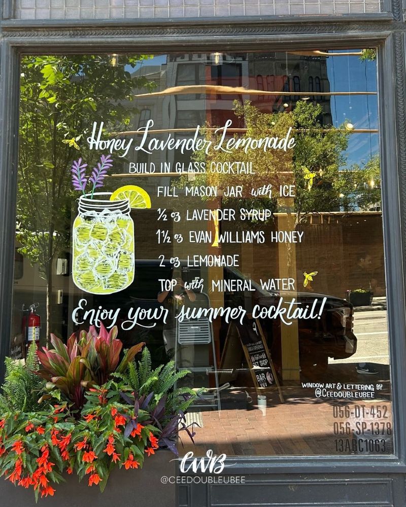 Hand lettered summer window display featuring a Honey Lavender Lemonade cocktail recipe for Evan Williams Bourbon Experience. Includes a detailed illustration of the drink and matching bees near the bottle branding.