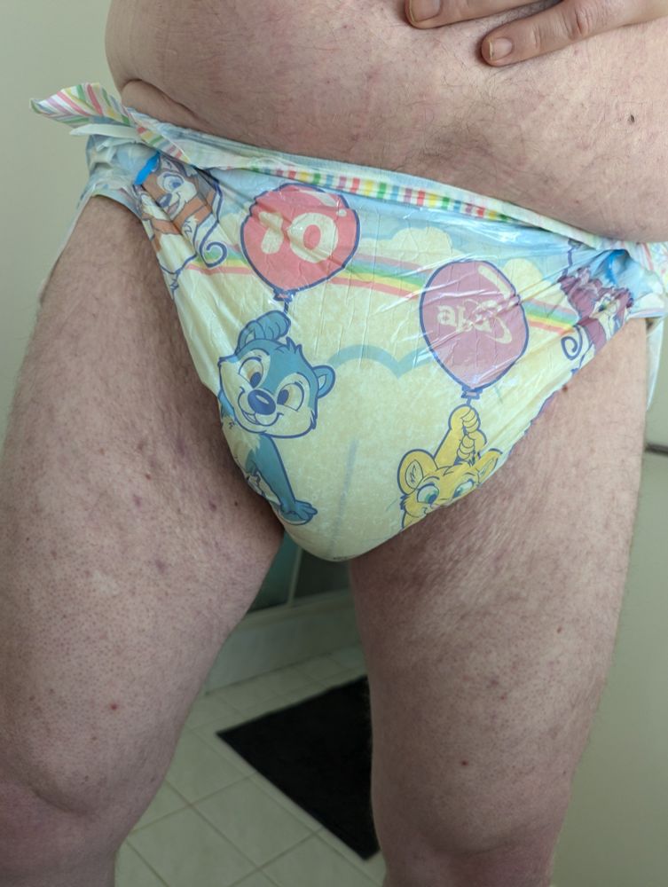 Front-on photo the crotch of a man wearing a TinyTails adult diaper. The entire front of the diaper is completely yellowed and splotchy. The wetness indicator stripe is completely blue and even faded in some spots. It is obvious the diaper is at 100% capacity, and it looks very soft and squishy.