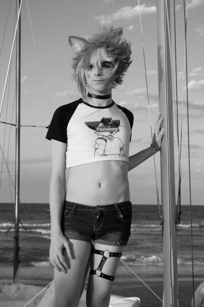 Me cosplaying as Gorou from Genshin impact in a femboy casual version. Laying against a pole from a boat at the beach, with the sea and clear sky behind me but in black and white 
