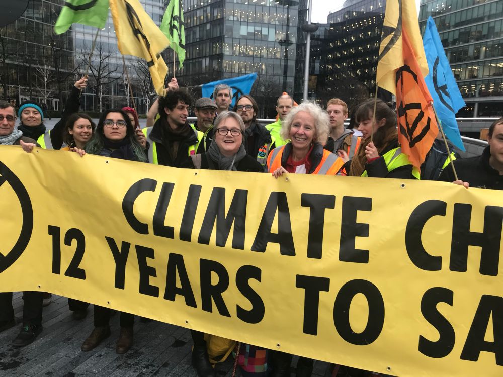 Big yellow climate banner with campaigners and XR flags outside old City Hall. 