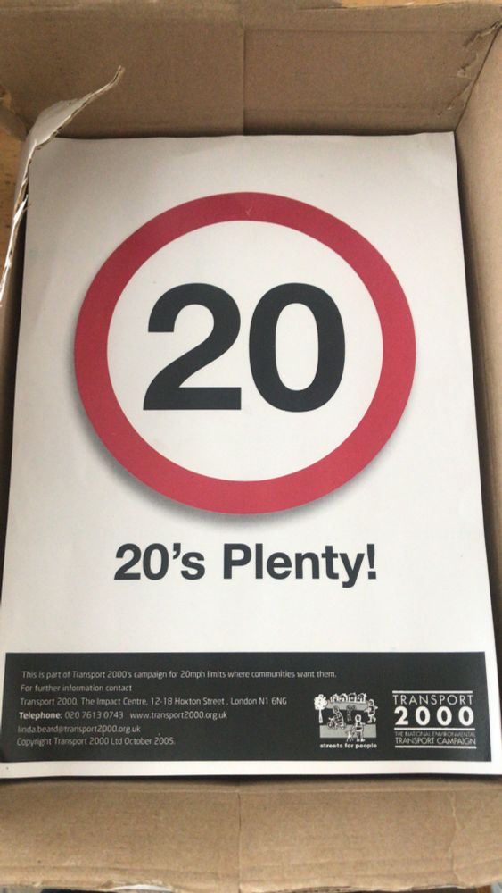 cardboard box with A4 posters saying 20 in black text in a red roundel and "20's plenty" underneath.

Black bar at bottom with "Transport 2000" now Campaign for Better Transport.