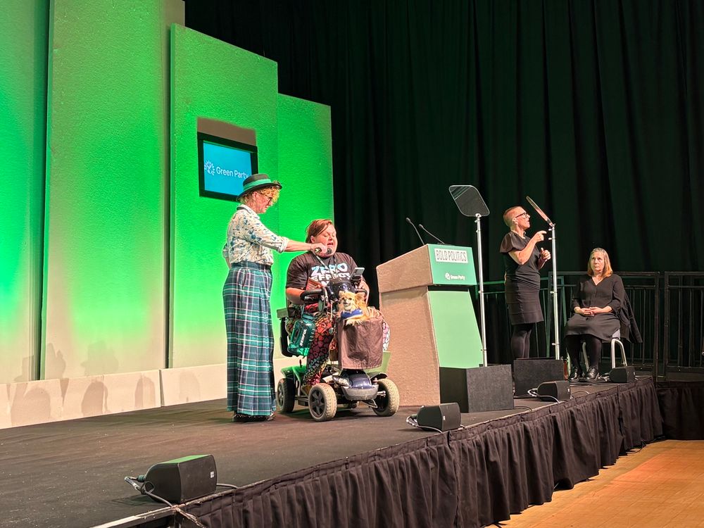 Cade with a dog on stage at Green conference with Ani in plaid trousers holding a mic