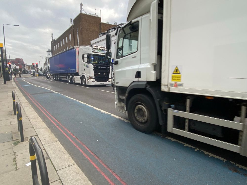 A faded blue bike lane with a huge white lorry encroaching across the white line with no wands to stop it. 