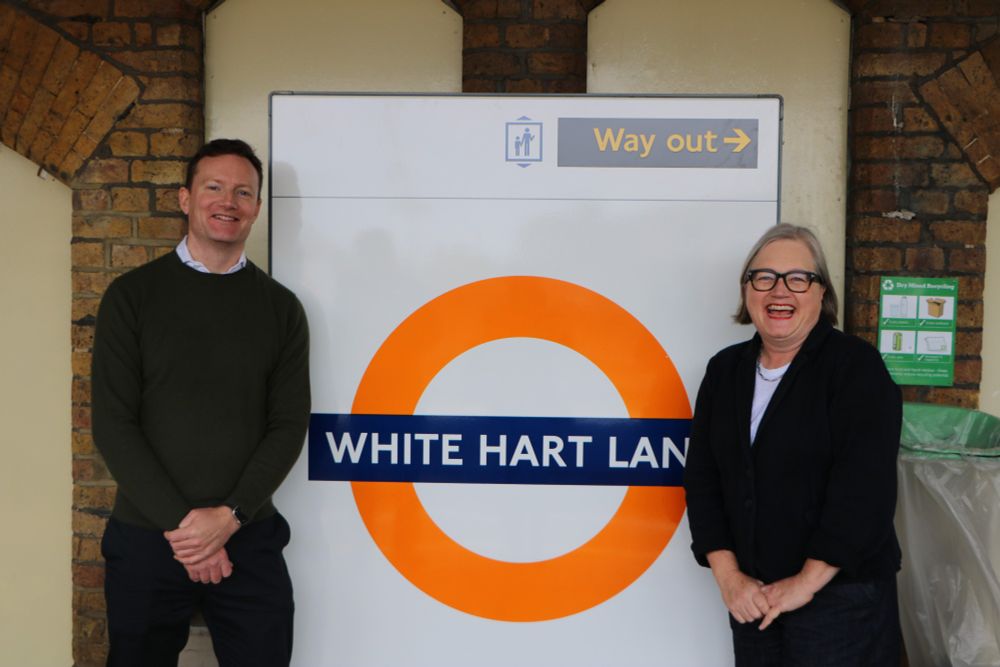 Seb Dandce Deputy Mayor for Transport and Caroline smiling by a White Hart Lane station roundel 