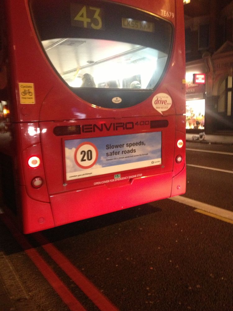 photo of the back of a red no 43 bus in 2014 carrying a sign "20" in a red roundel against blue sky with text "slower speeds safer roads"