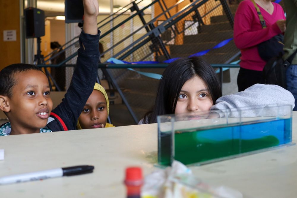 Three children, one with his hand raised, look at a tub of blue and green-colored water at the UW Aquatic Sciences Open House