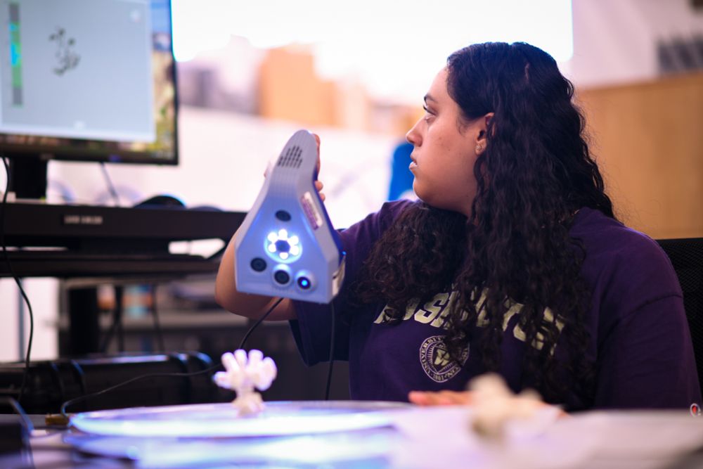 Eliana Shankar holds a state-of-the-art scanner over a piece of coral, while looking back at the image on the computer screen