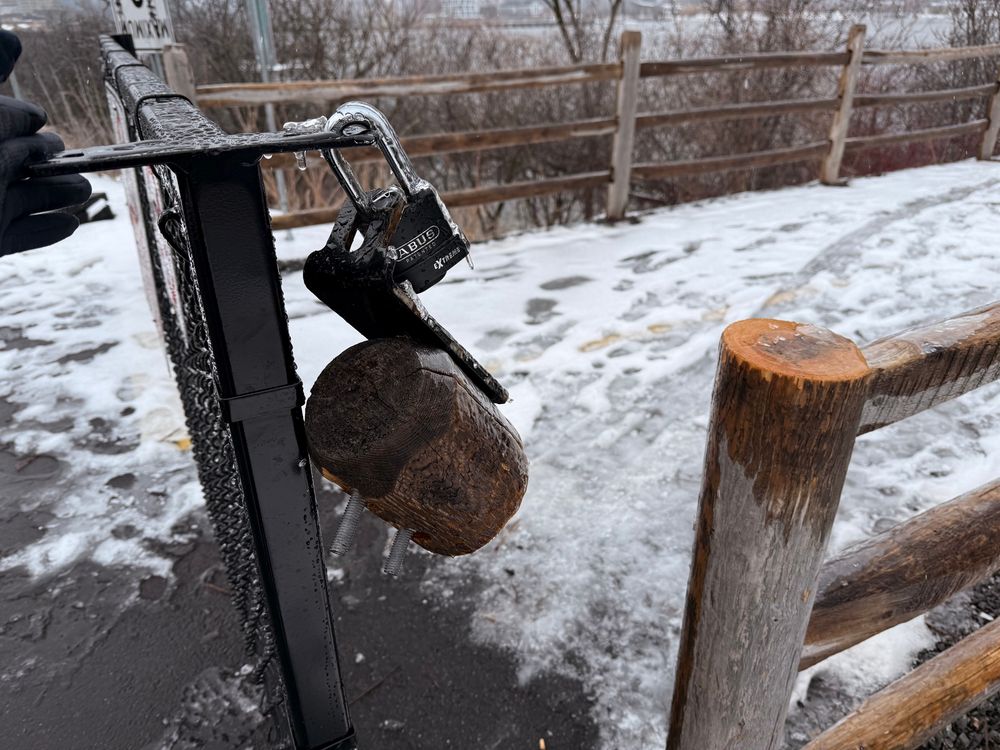 A locked gate blocks a pedestrian path. Someone sawed the post holding one end of the gate, allowing it to open (a different angle)