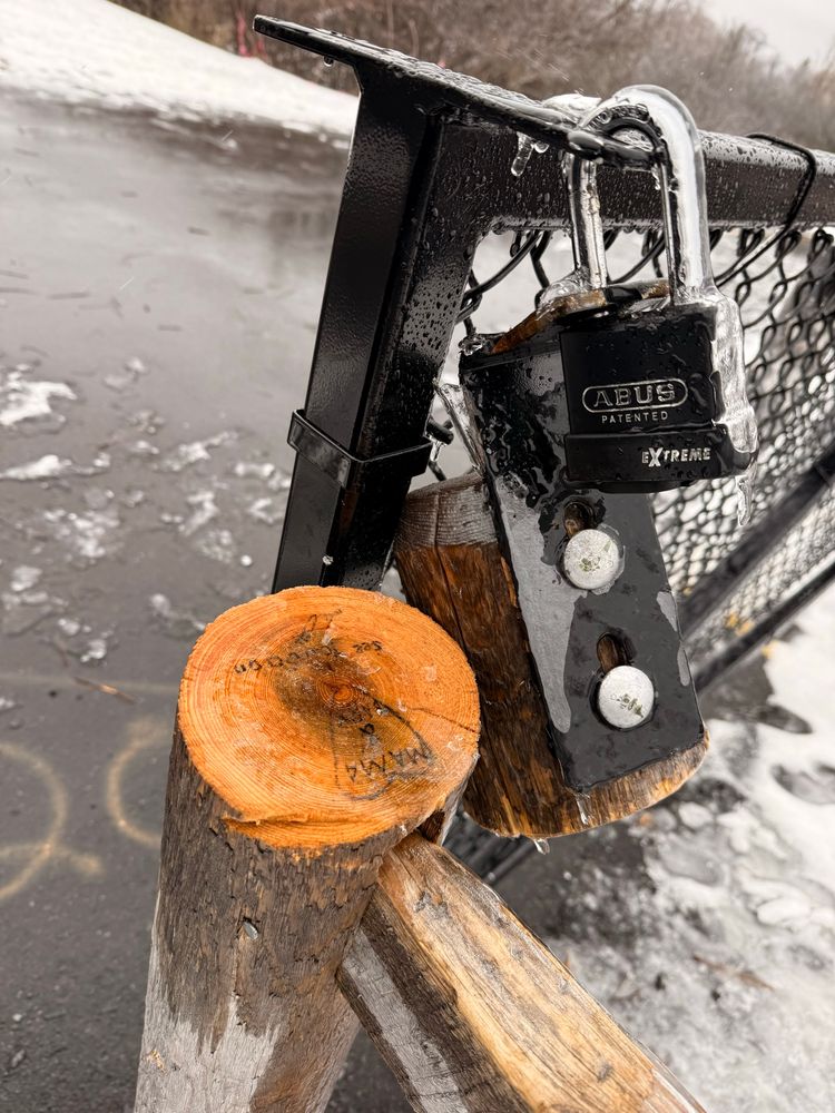 A locked gate blocks a pedestrian path. Someone sawed the post holding one end of the gate, allowing it to open 