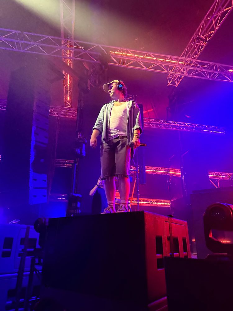 Fox Stevenson standing on the stage ontop of a big black box, looking down into the crowd. He is wearing silent disco headphones