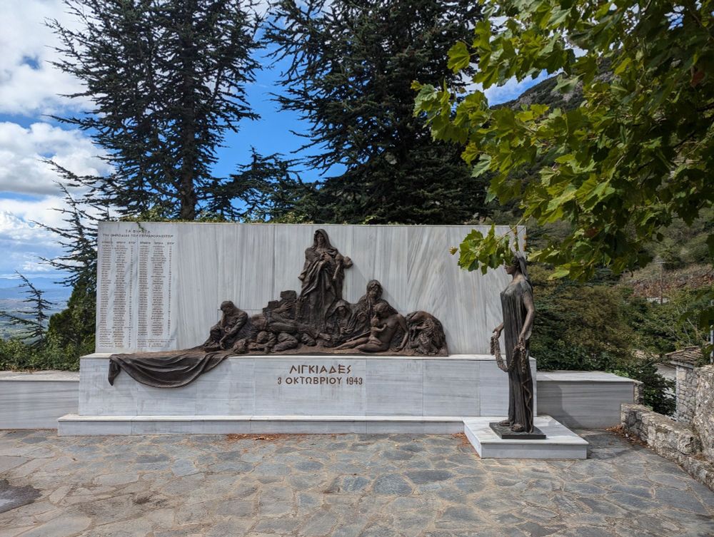 Gedenkwand zur Erinnerung an die Ermordeten von Lingiades, auf der linken Seite die Namen und das Alter der Ermordeten, rechts Skulptur, die an die Ermordeten erinnert