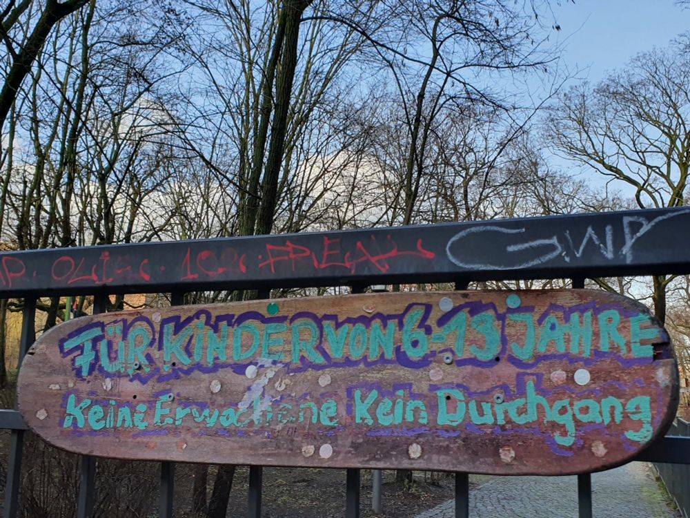 Schild an Zaun, dahinter Bäume. Auf dem Schild steht: Für Kinder von 6 bis 13 Jahre  Keine Erwachsene  Kein Durchgang
