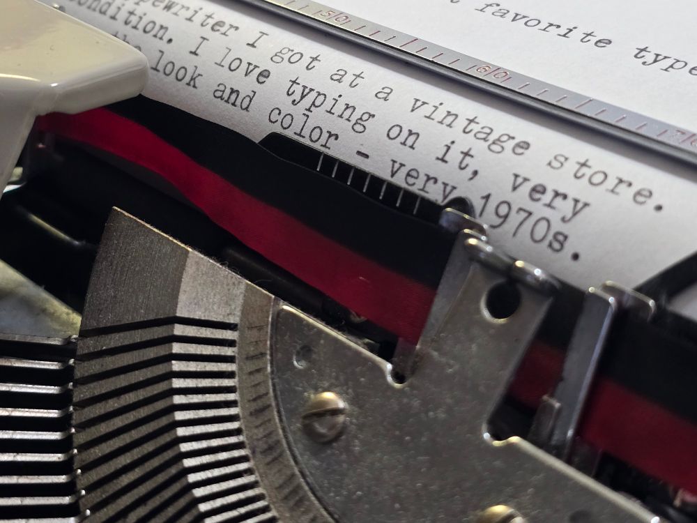 A close up of a Royal Mercury type writer, the typebar escapement, ribbon vibrator is visible with text typed onto the page describing my love for the styles and aesthetics of the 1970s.