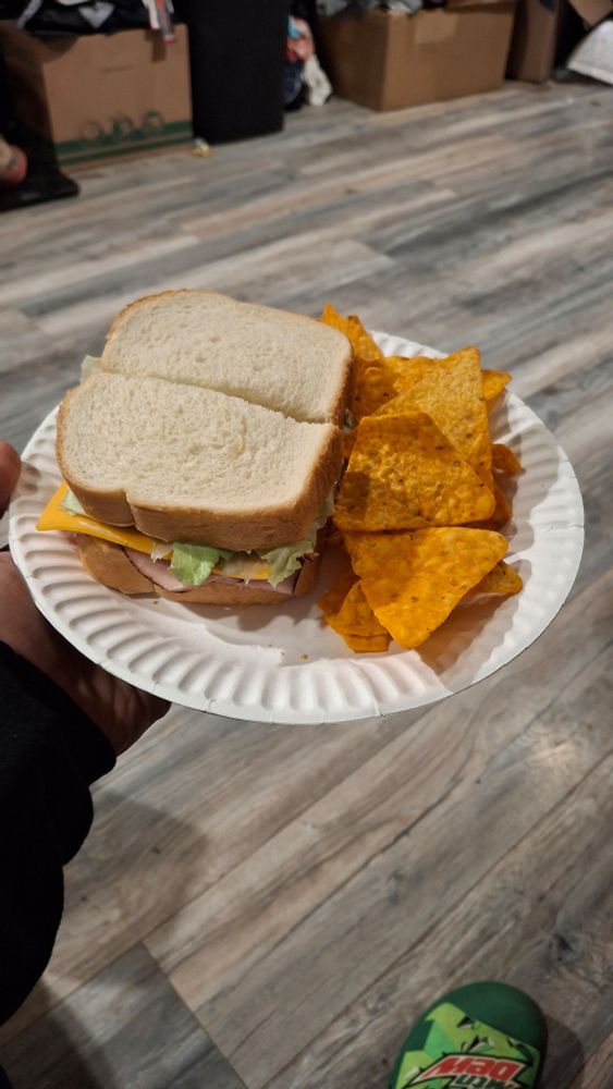 A ham and cheese sandwich, with lettuce, cut in half with a side of nachos cheese doritos sitting on a thin paper plate