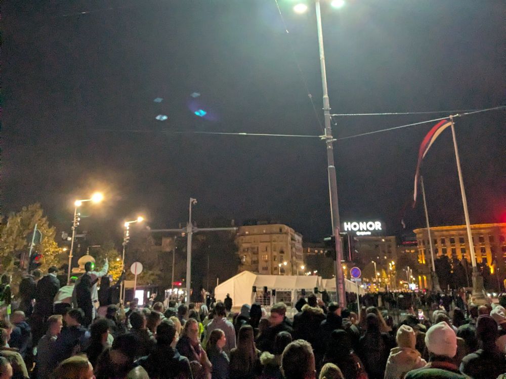 Belgrad, vor dem Nationalparlament, im Dunkeln. Gegen die Regierung Protestierende blicken in Richtung der inszenierten pro-Regierungs-Demo in großen weißen Zelten, aus denen heraus Laserpointer auf die Protestierenden gerichtet werden.