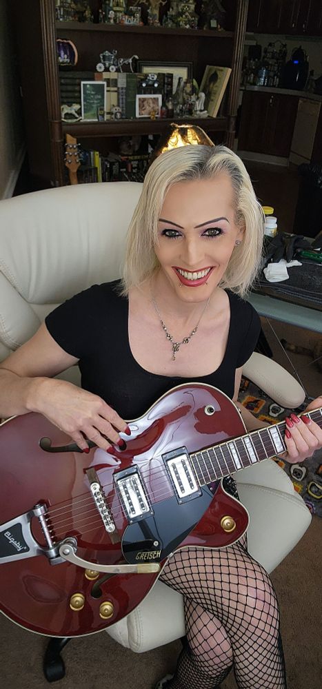 Tsarina Eve sitting in a white chair playing her Gretsch hollowbody streamliner while doing SW !
