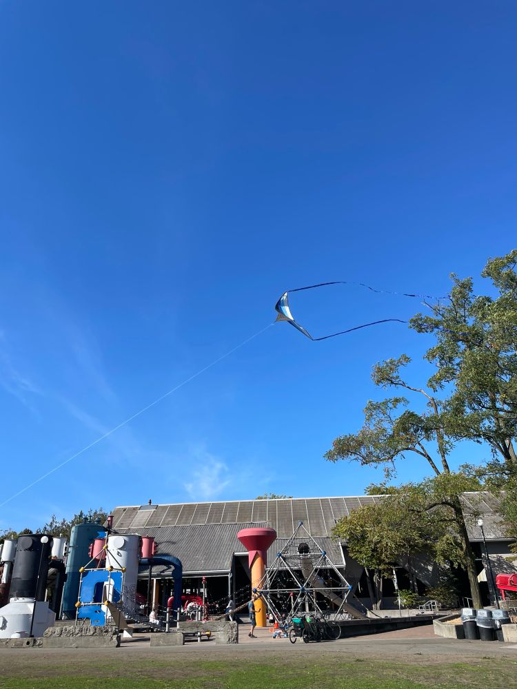 a kite in the sky above a playground at gas works park, the sky is beautiful blue and clear