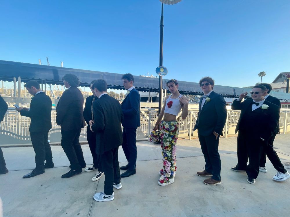 a line of young men in formal, dark suits and one giving c*nty Spring, with flowers covering bottom to waist and a heart formed out of red roses on a cropped white tank