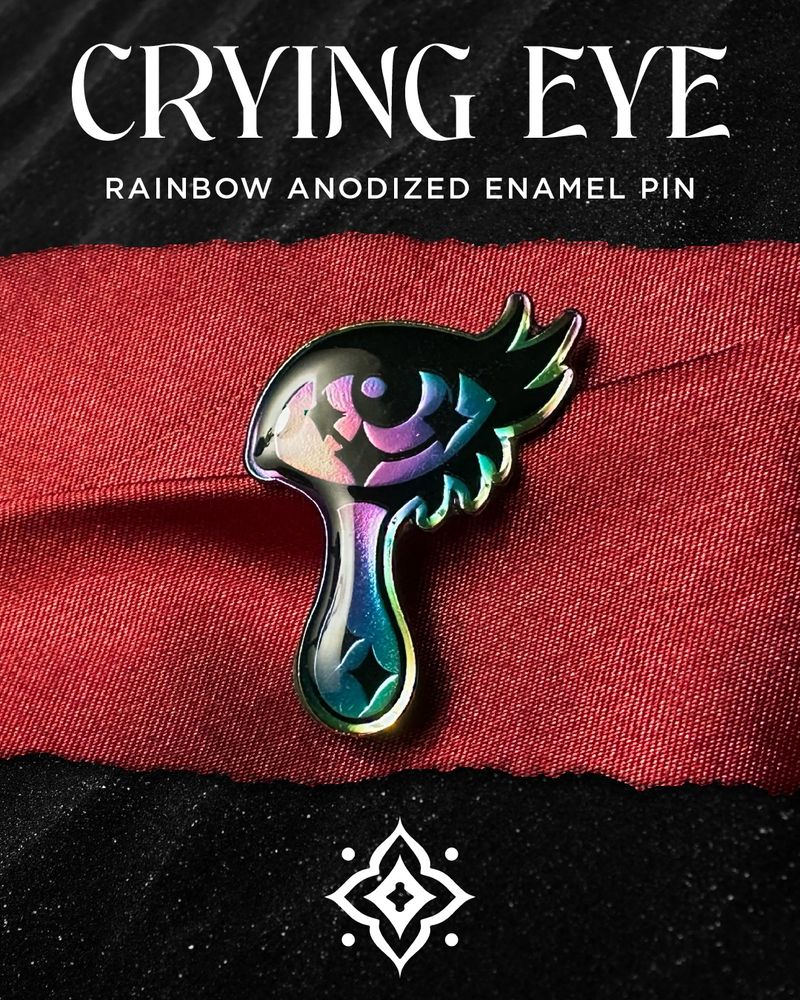 Photo of a rainbow metal lapel pin of a feminine eye with a large teardrop descending from it. There are sparkle highlights within the eye and teardrop. Text above reads: "Crying eye rainbow anodized enamel pin." The artist's logomark is below.