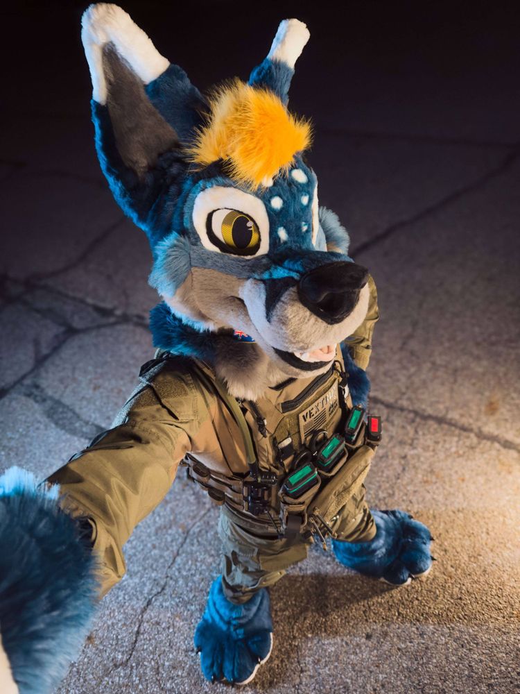 Fursuiter in tactical wolf gear striking a confident, playful pose for #FursuitFriday.
