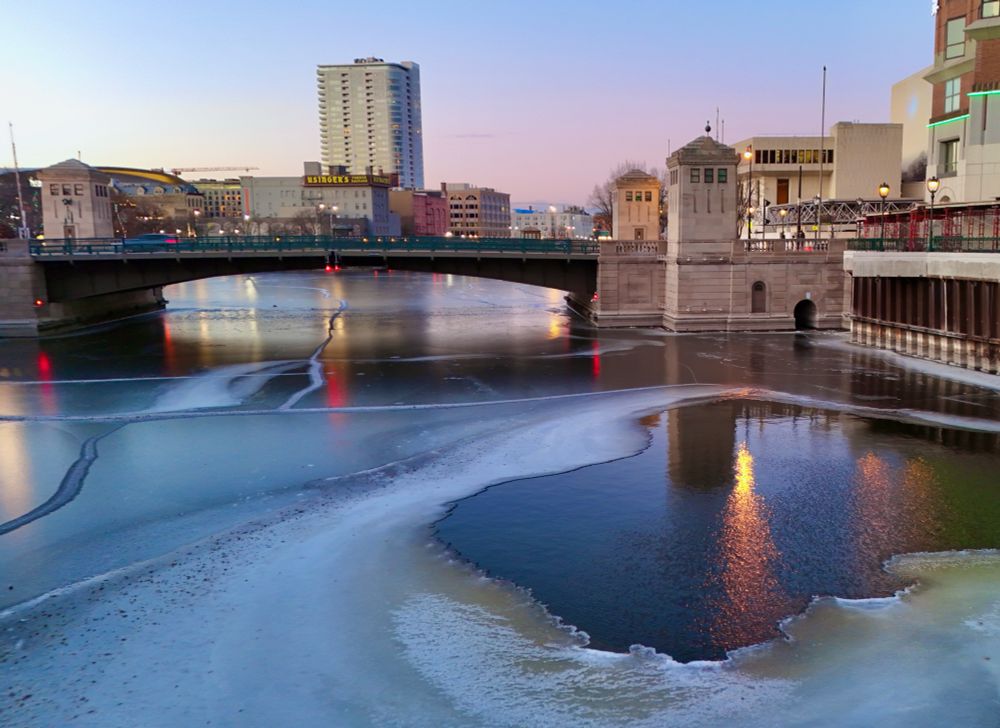 Icy river in the foreground of a bridge within a city of varied types of buildings 